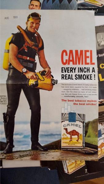 A man in SCUBA gear smokes a cigarette next to the water.
